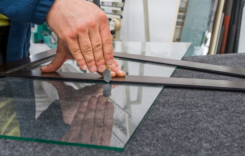 Glazier carefully cutting glass for a window frame
